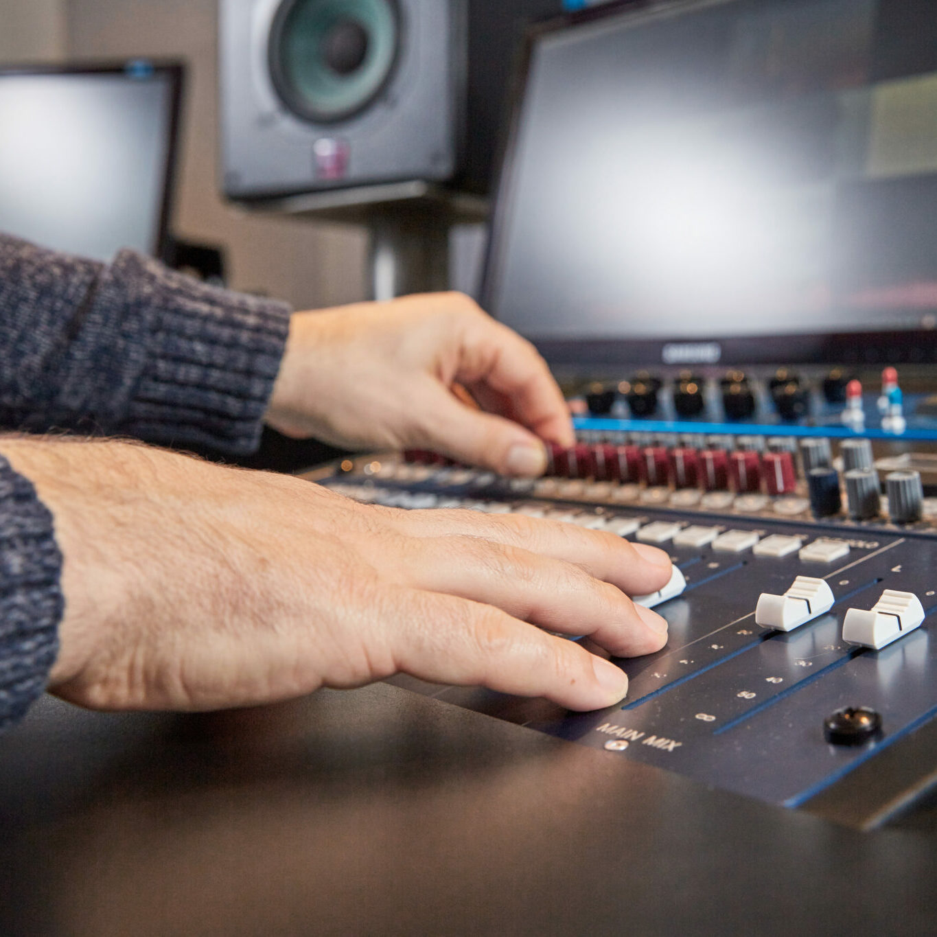 Audio equipment and computer monitors in a sound studio with hands of the music producer on the mixing desk